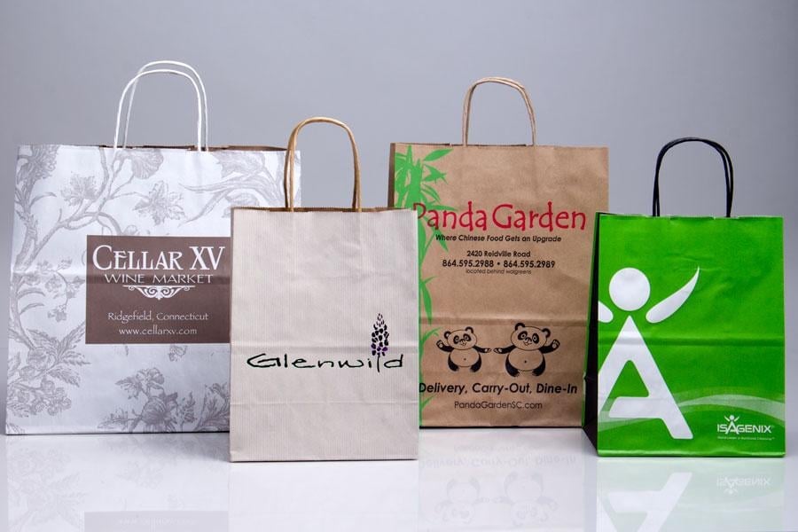 Four branded shopping bags with handles displayed in a row: white floral Cellar XV bag, beige Galerias bag, tan Panda Garden bag, and bright green bag with white logo